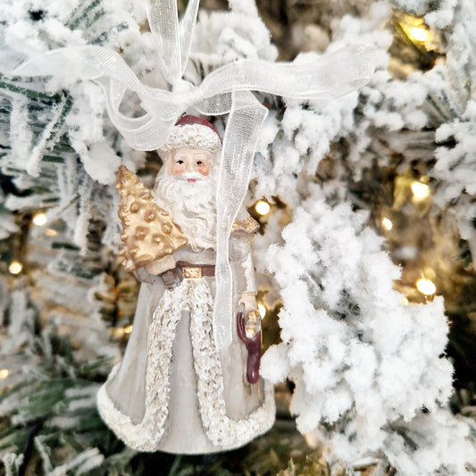 santa dressed in white holding a gold tree christmas decoration on a white ribbon