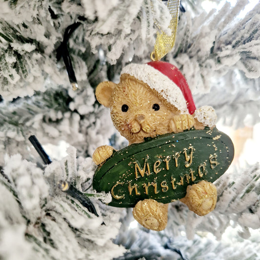 Teddy bear holding a merry christmas sign hanging on a gold ribbon christmas tree decoration