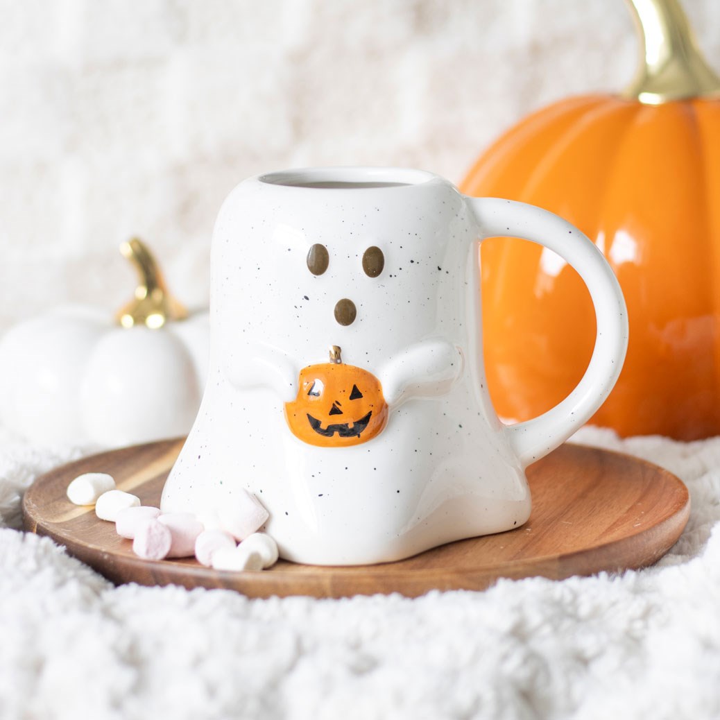 white ghost shaped mug with speckled detail holding a small orange pumpkin