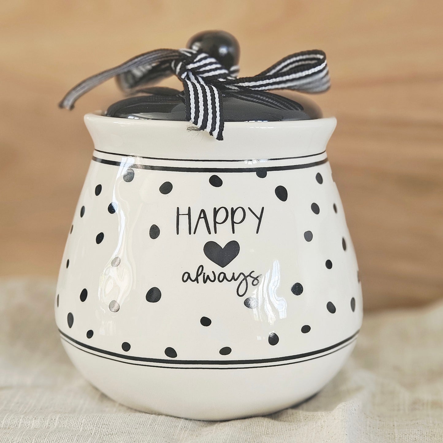 White ceramic jar with black polka dots and text, tied with a black and white striped ribbon, happy always text