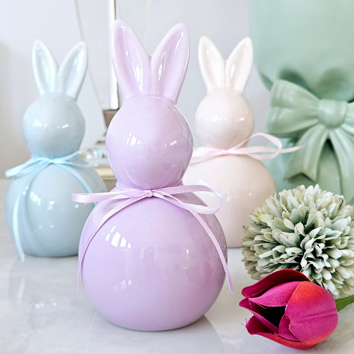 Three ceramic bunny figurines in pastel colours with a pink bow