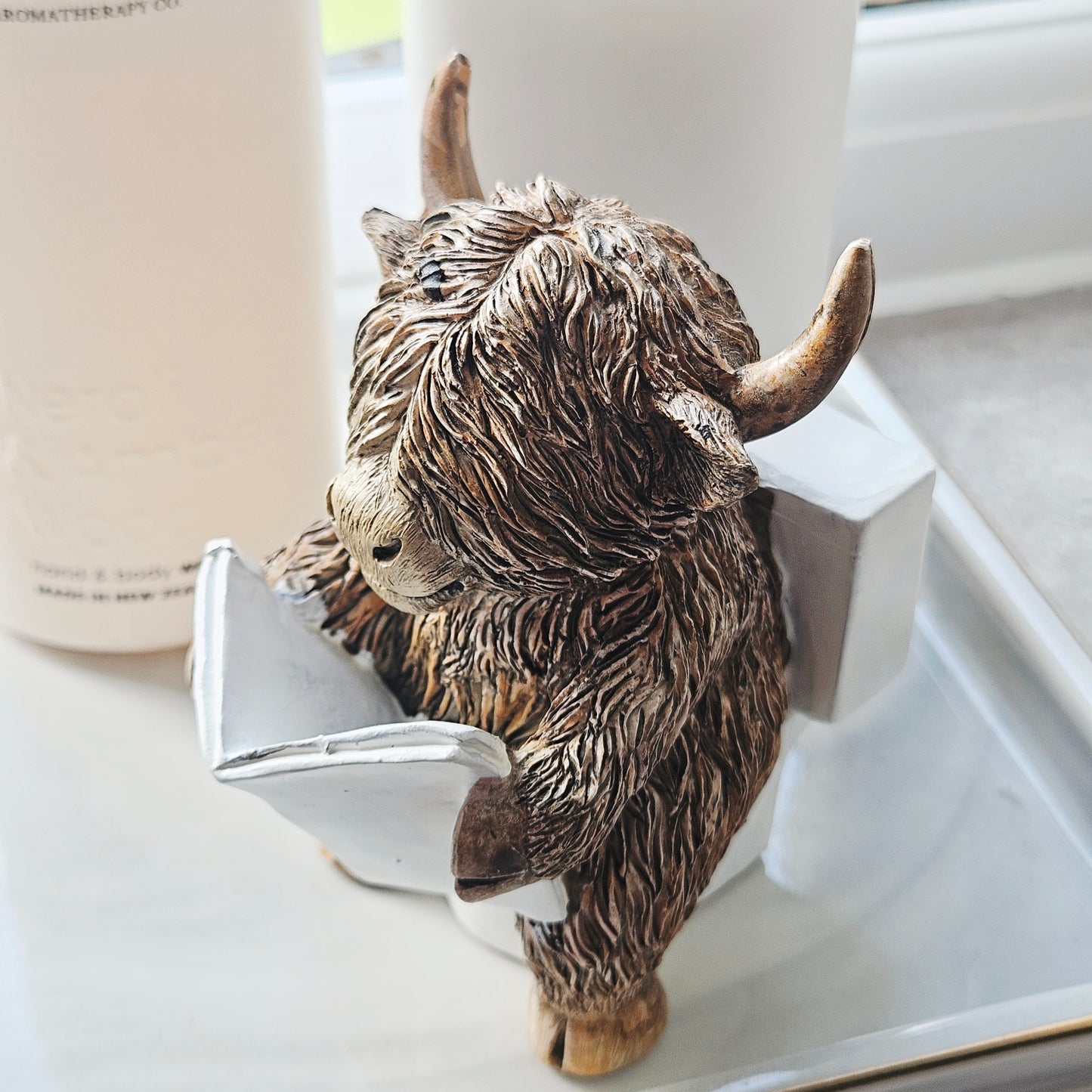 Statue of a Highland cow reading a book sitting on a toilet