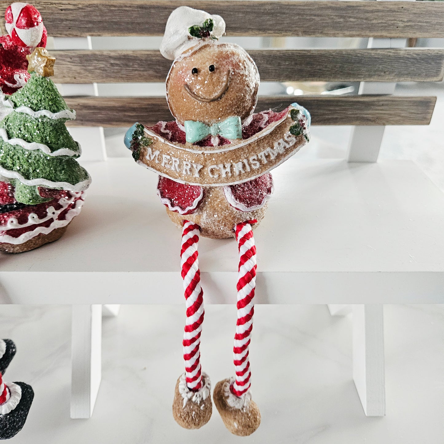 Decorative gingerbread man with candy cane legs holding a 'Merry Christmas' sign