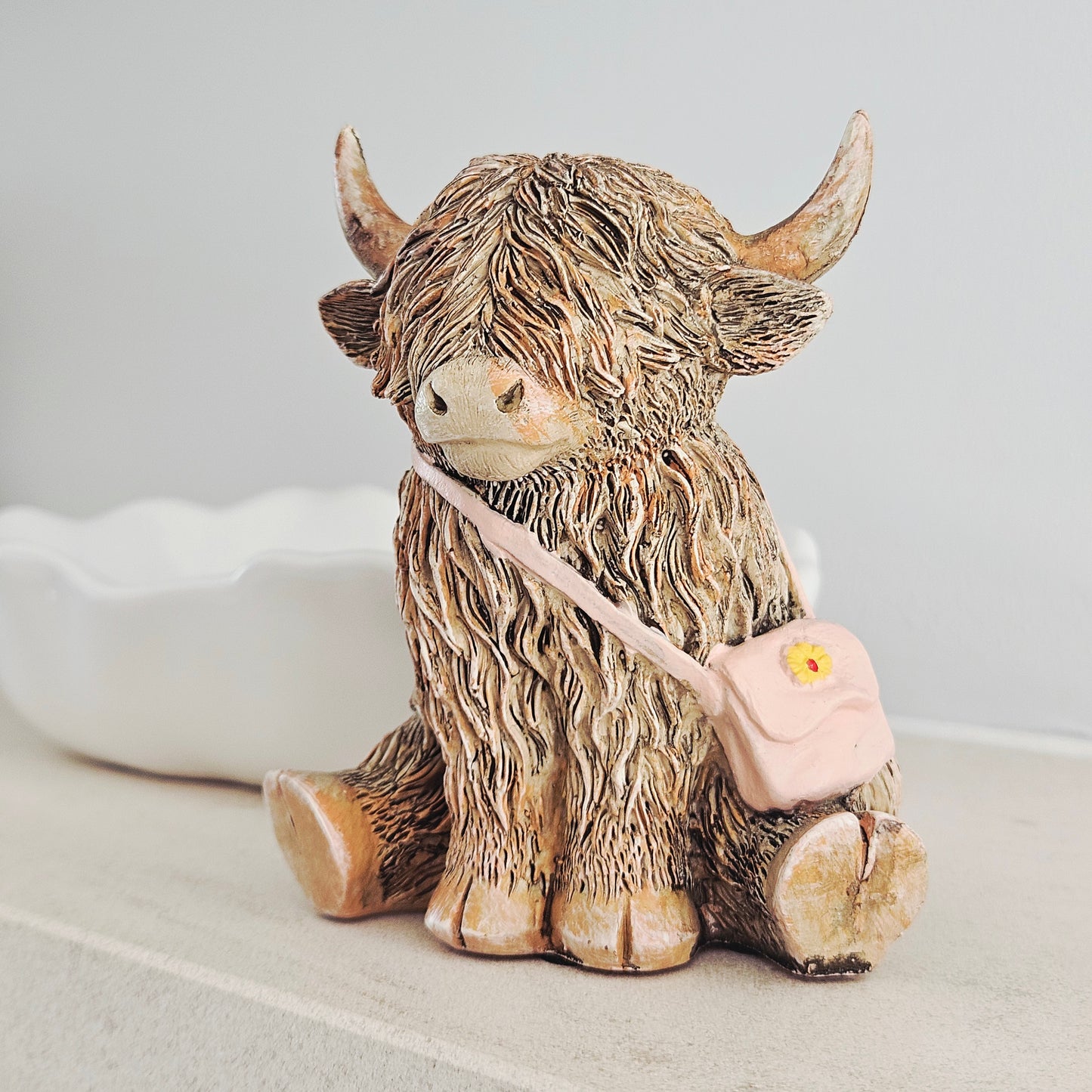 highland cow ornament wearing a pink handbag with yellow flower