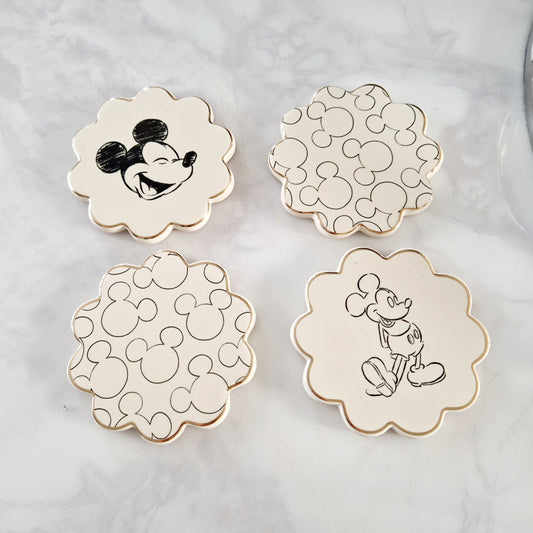 four ceramic coasters featuring a gloss, cream finish, complete with gold coloured edging and individual Mickey Mouse printed designs. 