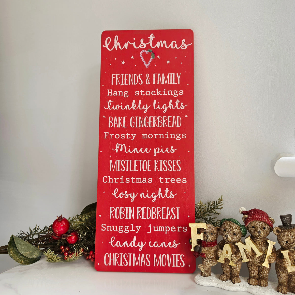 A red rectangular wooden sign with white script text listing Christmas activities and phrases
