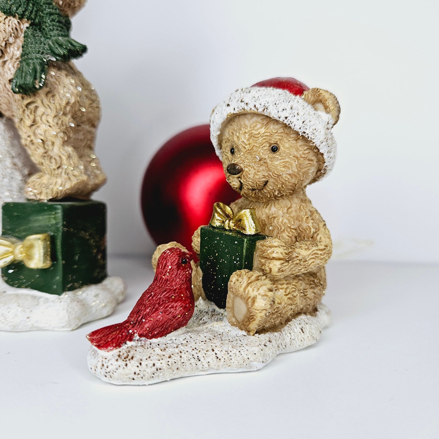 teddy ornament wearing a Santa hat holding a green present with gold bow with a red bird