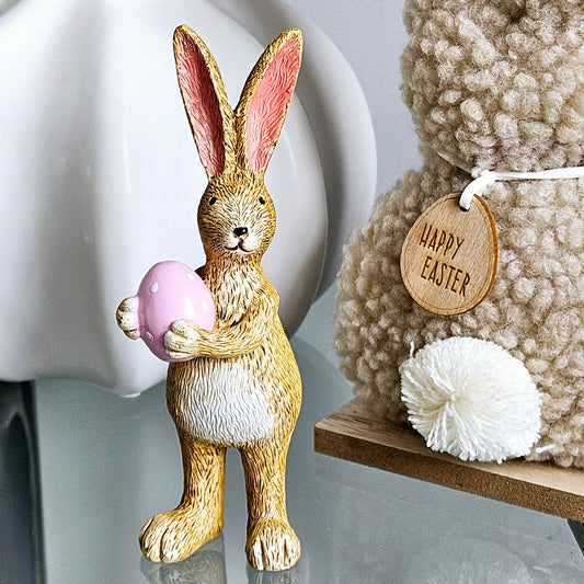 Standing rabbit ornament holding a pink egg with white spots