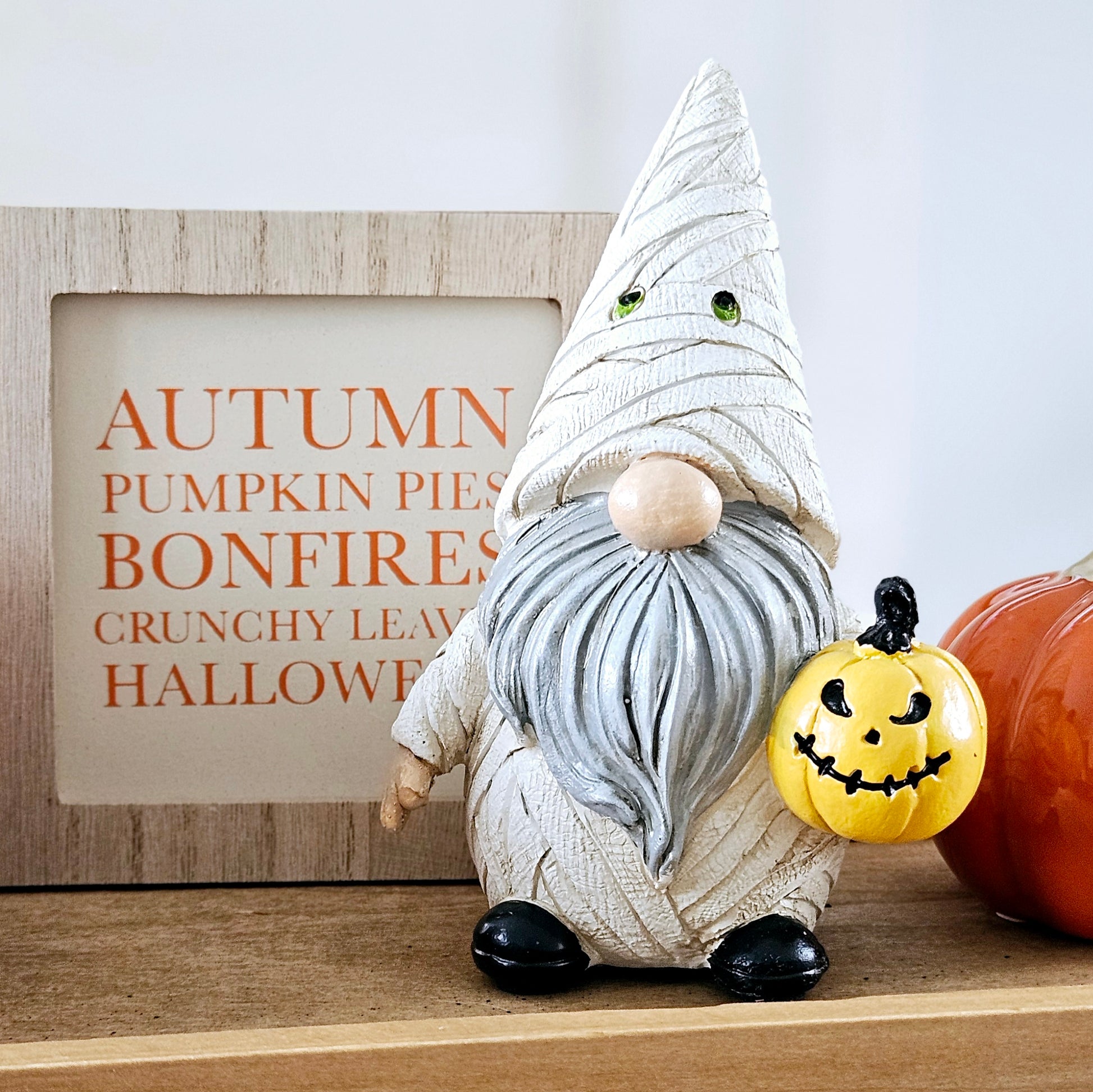 gnome ornament dresses as a mummy for halloween all in white holding an orange pumpkin