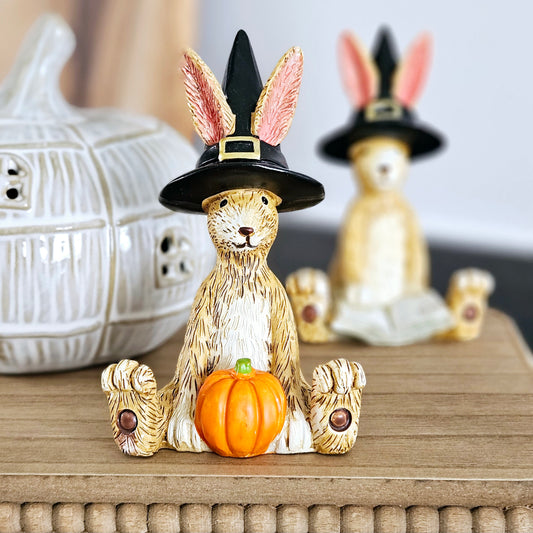 halloween sitting witch rabbit holding an orange pumpkin and wearing a witches hat