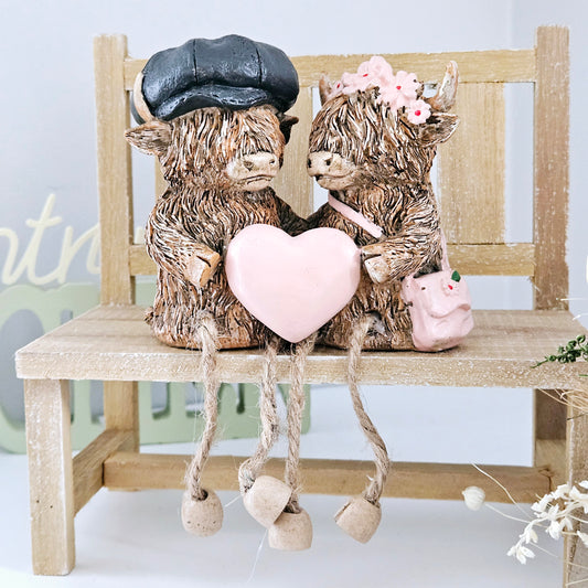 Highland cow duo Ornament holding a pink heart with pink flower hairband and bag and boy with blue hat 