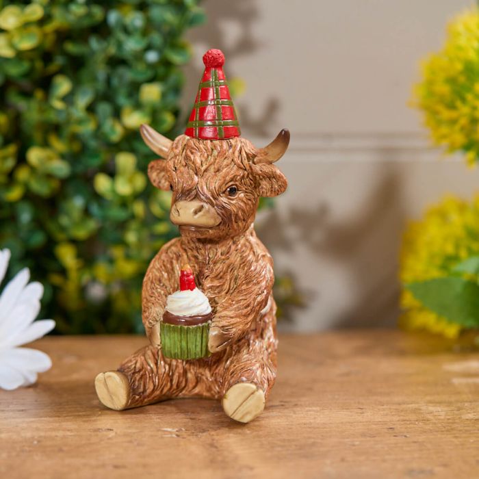 highland cow ornament holding a cupcake and wearing a red and Green Party birthday hat