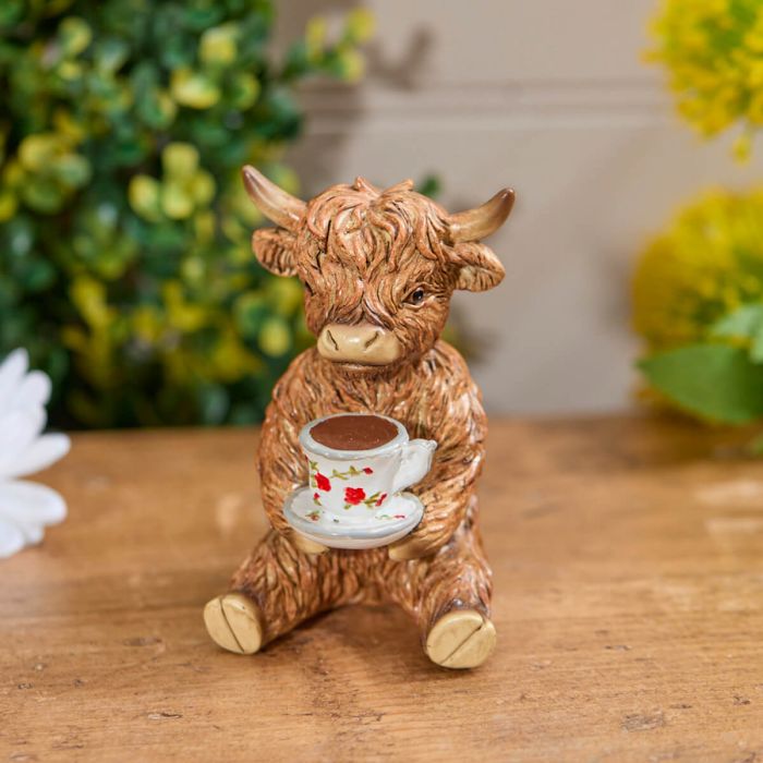 highland cow resin ornament sitting down holding a cup of tea in hands