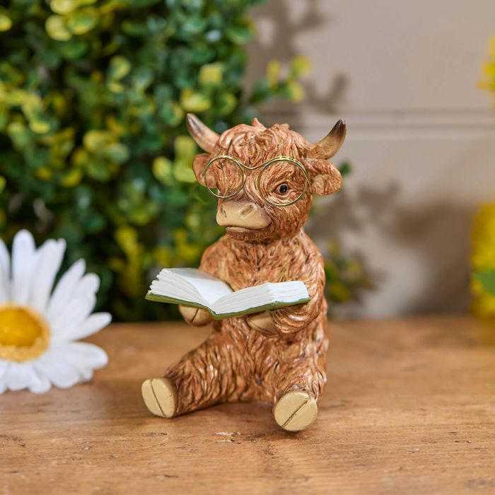 highland cow resin ornament reading a book and wearing green framed glasses 