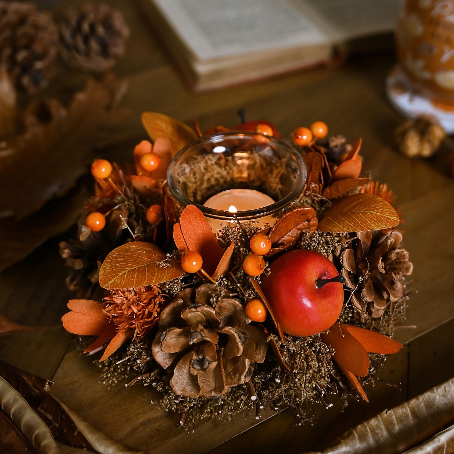 Decorative fall candle holder arrangement with candles, apples, and pinecones on a wooden surface.