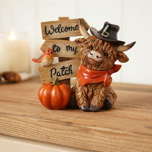 Decorative figurine of a cow with a pilgrim hat and pumpkin, standing next to a wooden sign. welcome to my patch