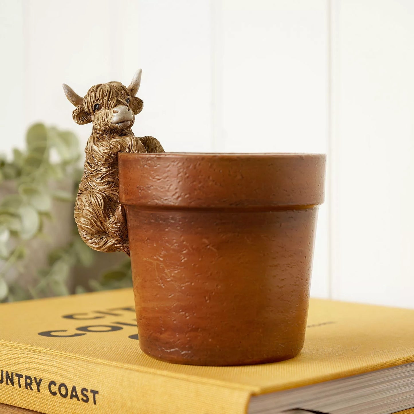 highland cow planter with figurine perched on the side of the brown pot