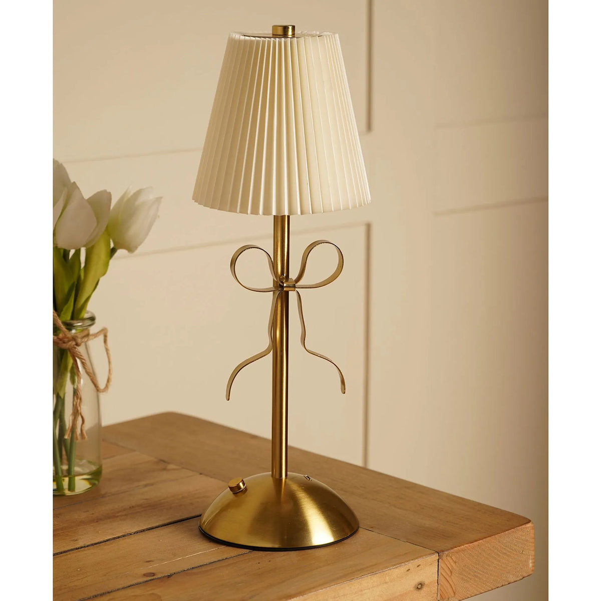 A brass table lamp with a pleated cream fabric shade and a decorative bow-shaped stem
