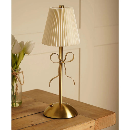 A brass table lamp with a pleated cream fabric shade and a decorative bow-shaped stem