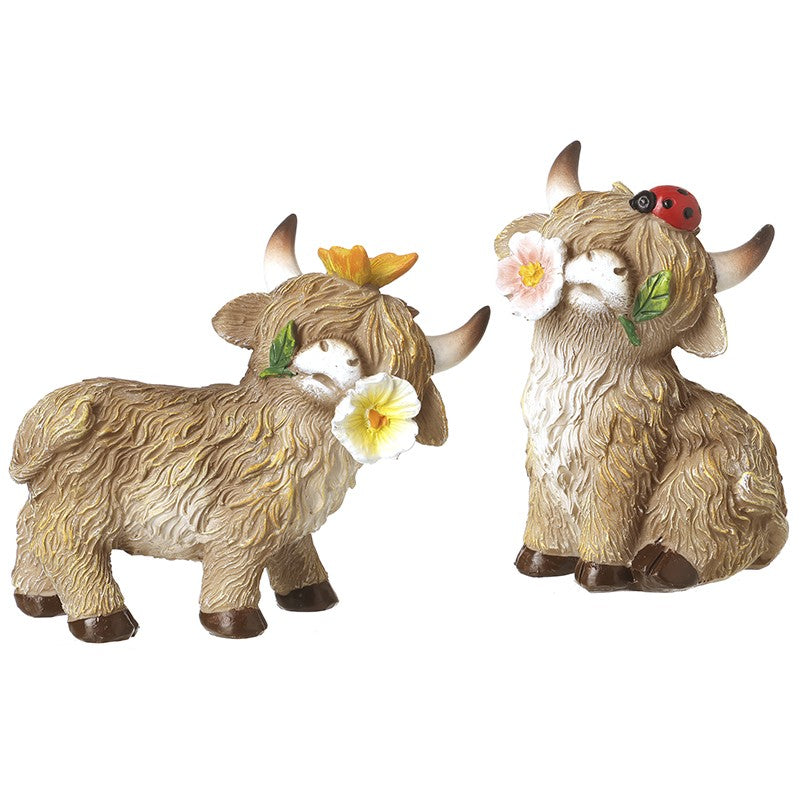 Two decorative statues of Highland cows with floral and ladybug accessories and butterfly