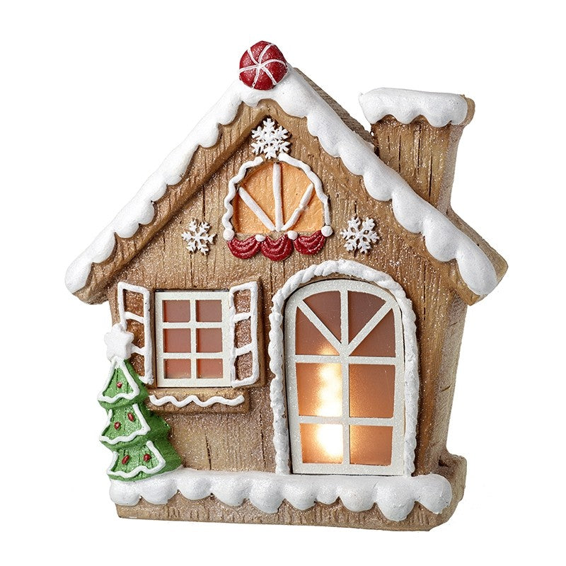 A gingerbread-style house ornament with faux snow around the roof and base, white-trimmed windows, a warm glowing window, red decorative accents, a small green Christmas tree, and a red-and-white striped ornament on top