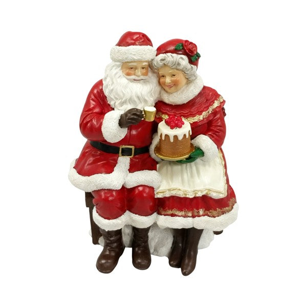 A Christmas figurine depicting Santa Claus and Mrs. Claus sitting together on a bench, holding a small cake.