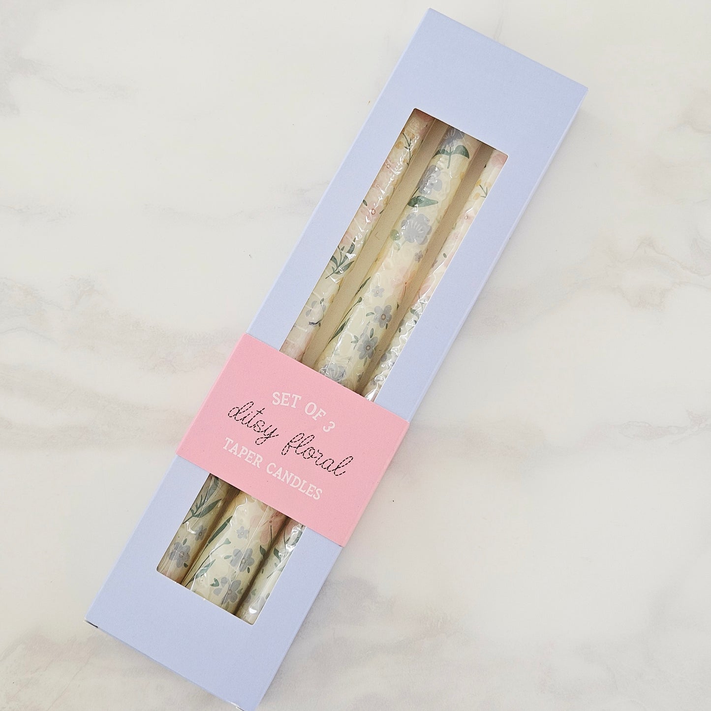 Set of three floral taper candles in a box with a pink label on a light gray background