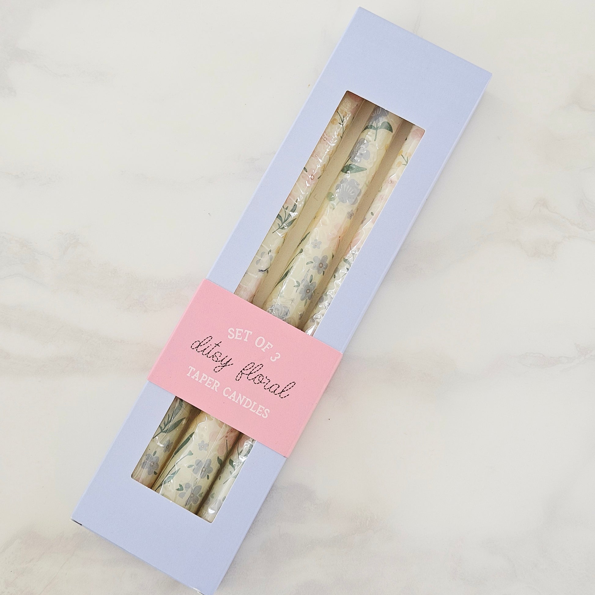 Set of three floral taper candles in a box with a pink label on a light gray background