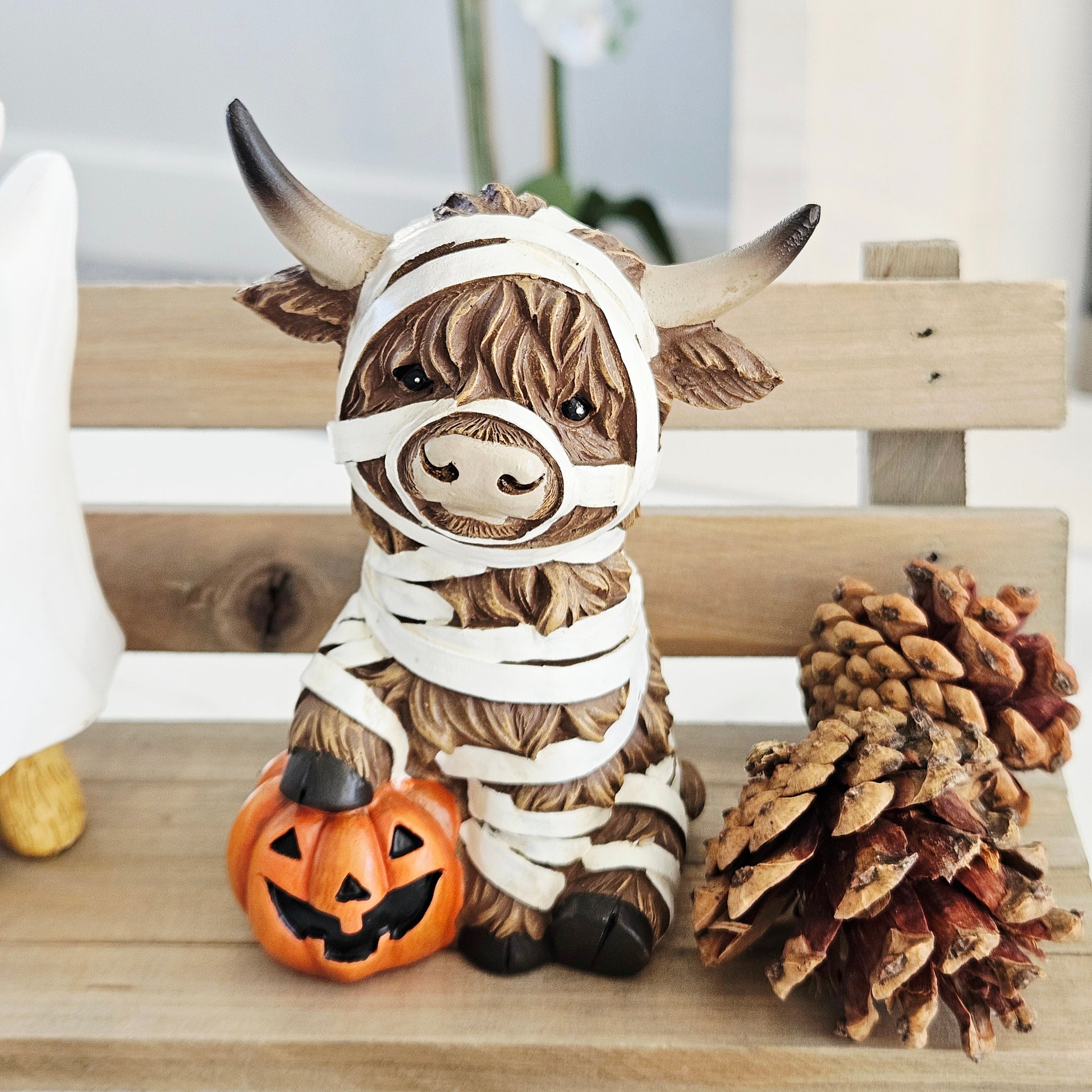 highland cow ornament dressed as a mummy with foot on a pumpkin 13cm