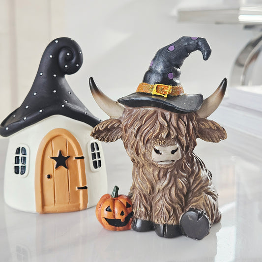 Ceramic highland cow figurine with a witch hat and pumpkin 