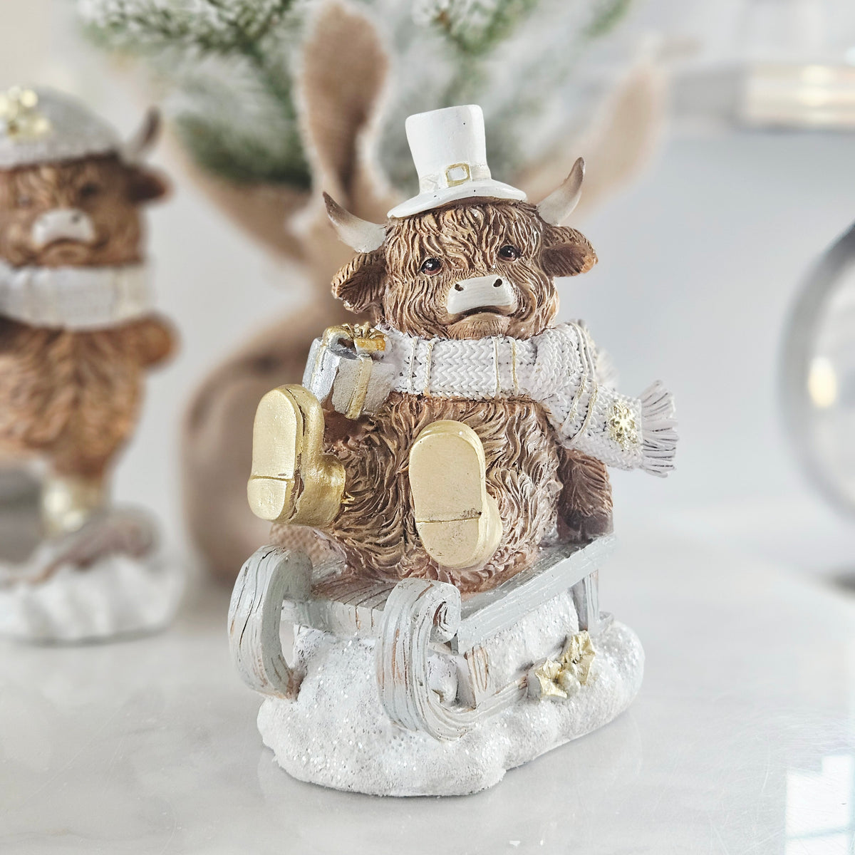christmas highland cow sitting on a sleigh with a white top hat and gold boots 15cm