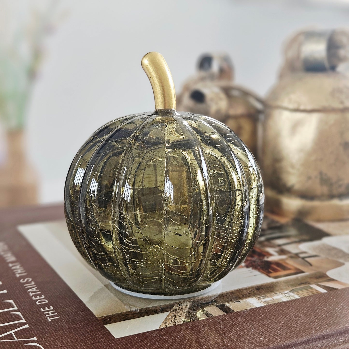 A decorative small ribbed glass led pumpkin in a smoky olive-green finish with a metallic gold stem, 