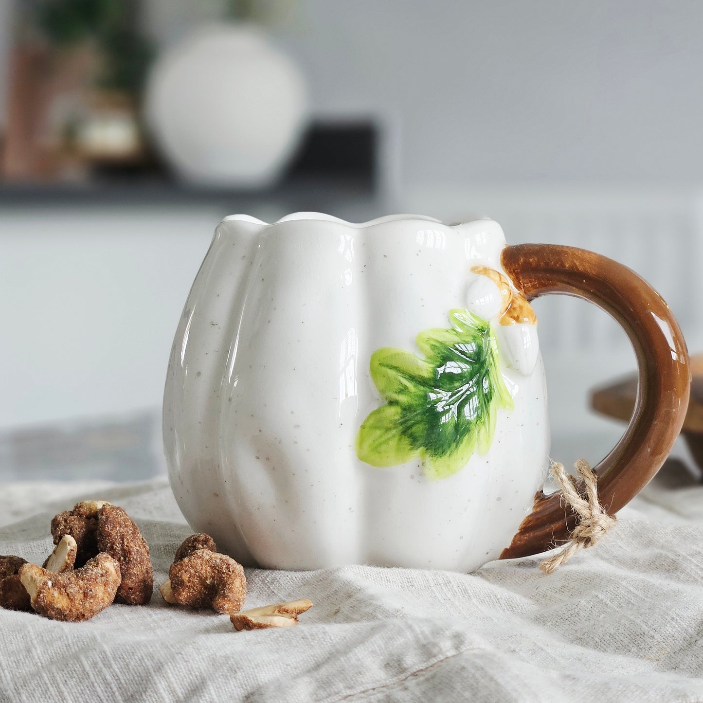 White ceramic pumpkin shaped mug with a brown handle and green leaf design & acorns