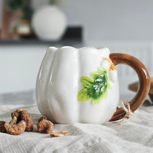 White ceramic pumpkin shaped mug with a brown handle and green leaf design & acorns