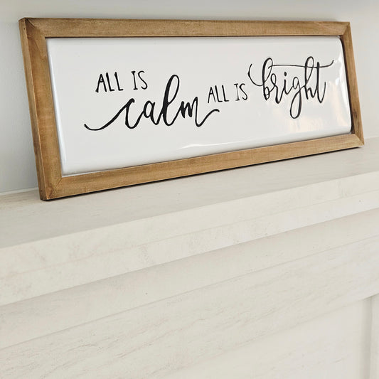 Wooden-framed sign with 'All is calm, All is bright' text on a white background made metal and wood