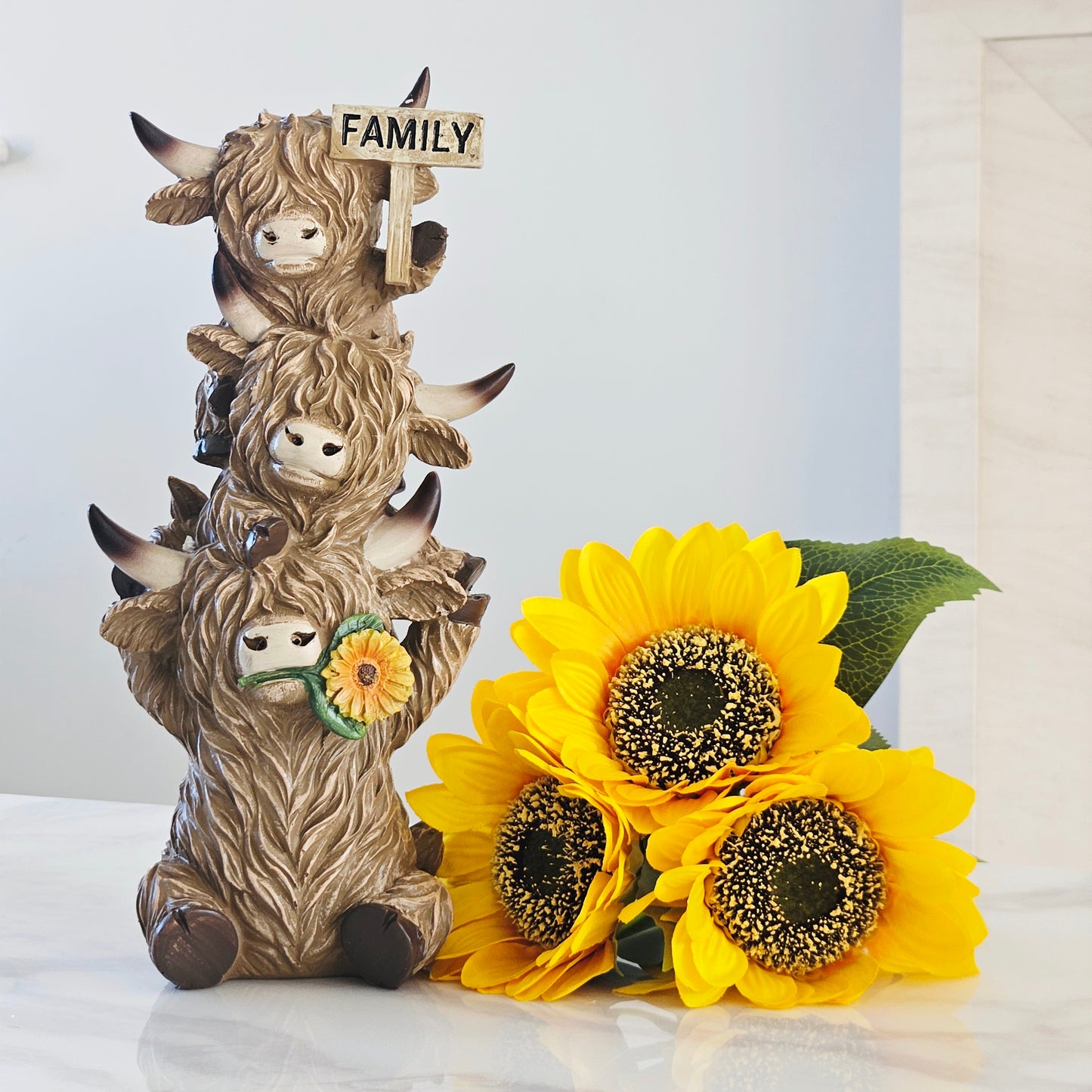 Decorative figurine of three stacked highland cows with a 'Family' sign and sunflowers 32cm