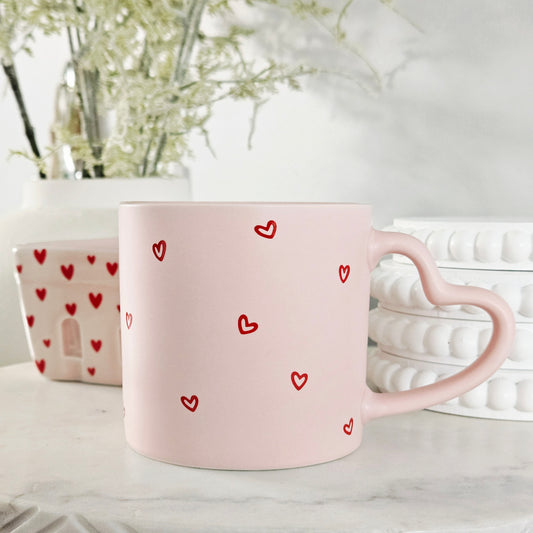 Pink mug with red hearts all over and amore written inside with a heart shaped handle 