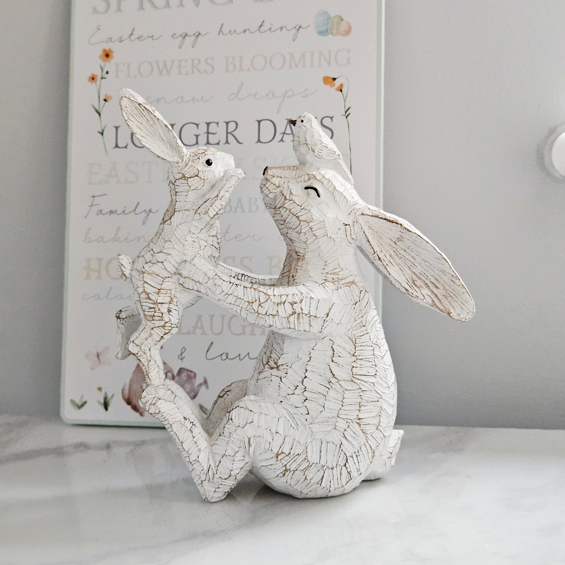 Decorative white rabbit figurine holding a baby rabbit and bird on mums head