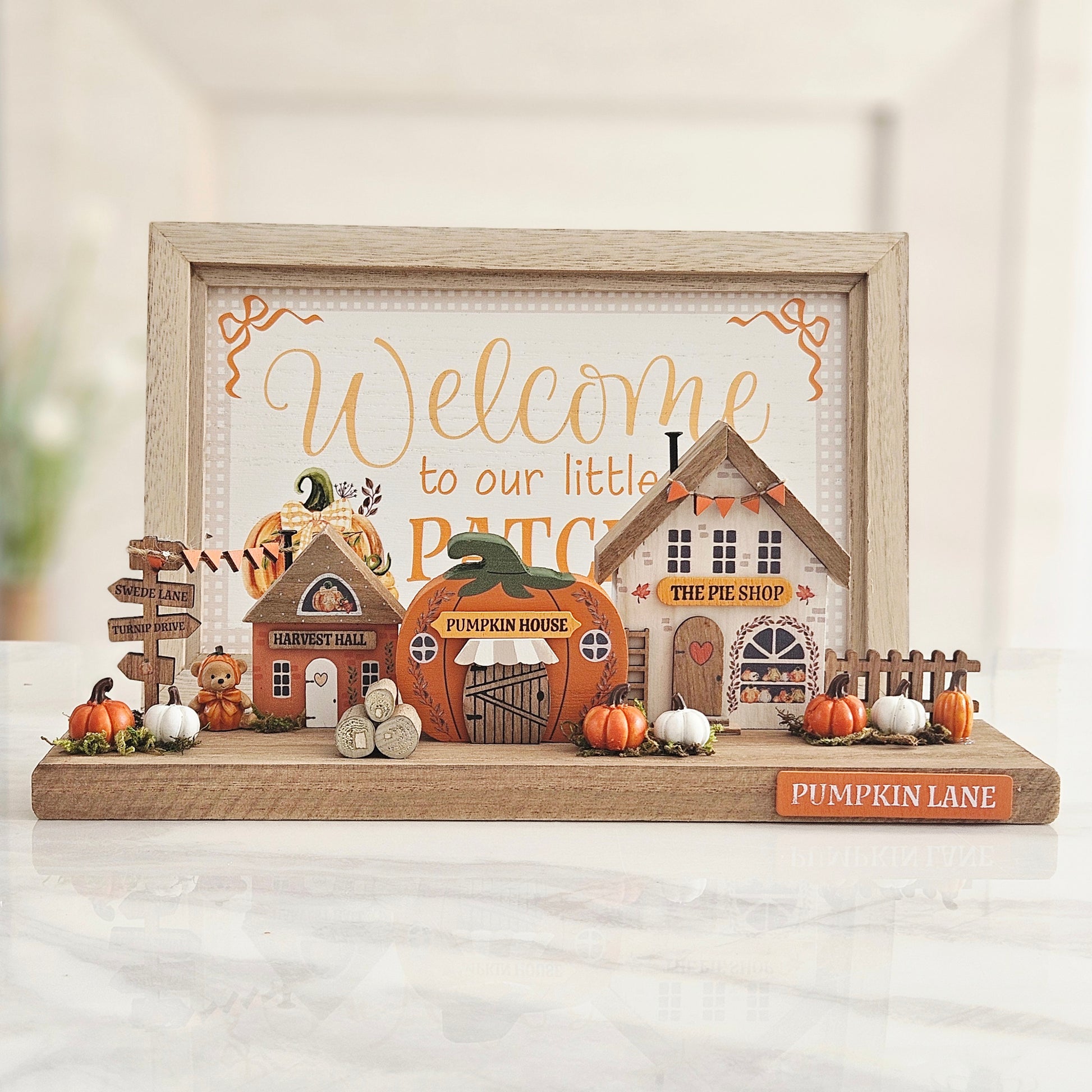 A framed autumn-themed tabletop display with miniature houses, pumpkins, a barn, and a sign reading  'Pumpkin Lane,' 