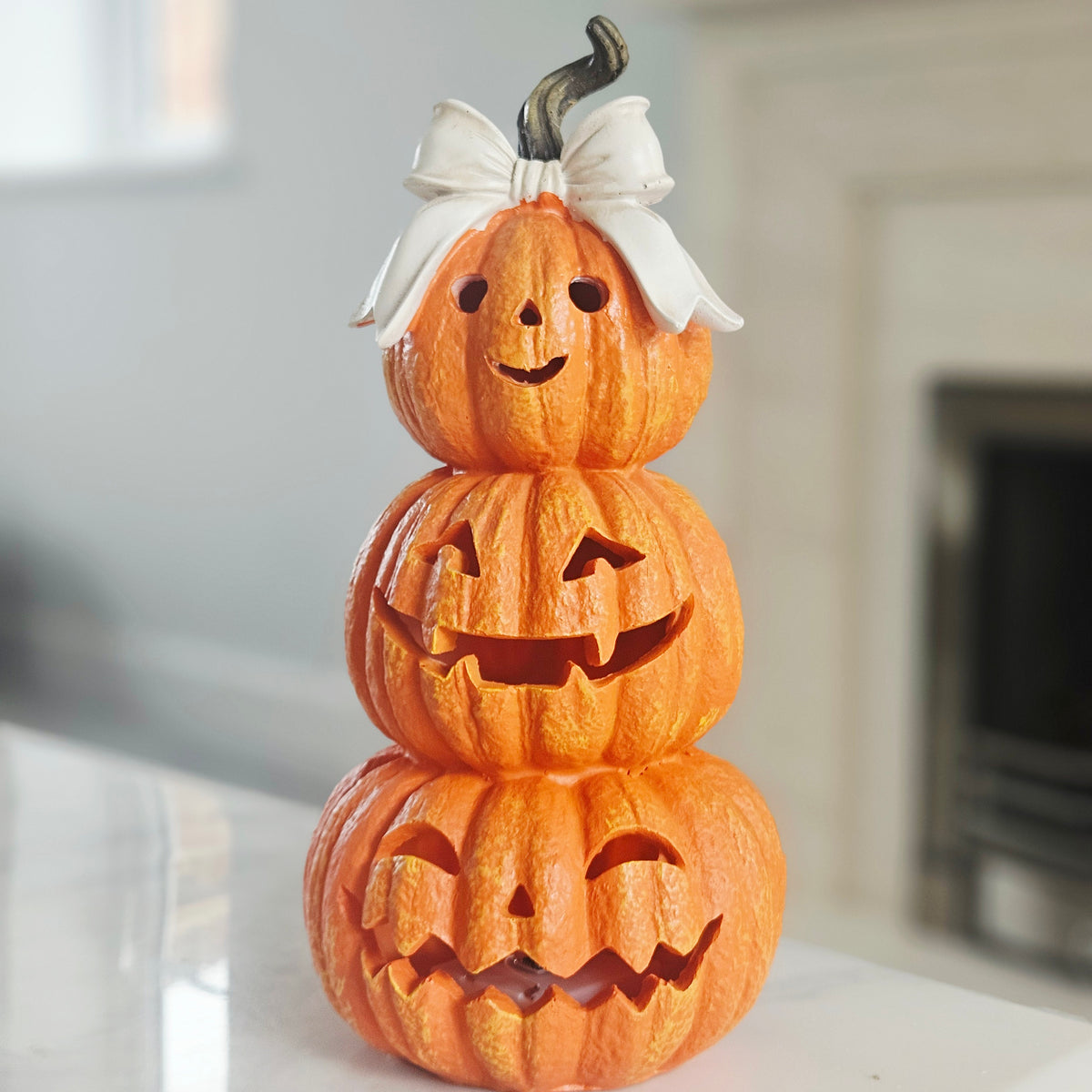 Three stacked jack-o'-lantern pumpkins with carved faces, topped with a white bow, with led lights 