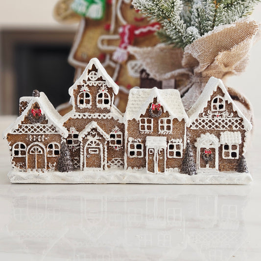 A decorative gingerbread village scene with four small brown house figures covered in white icing-like detailing, 