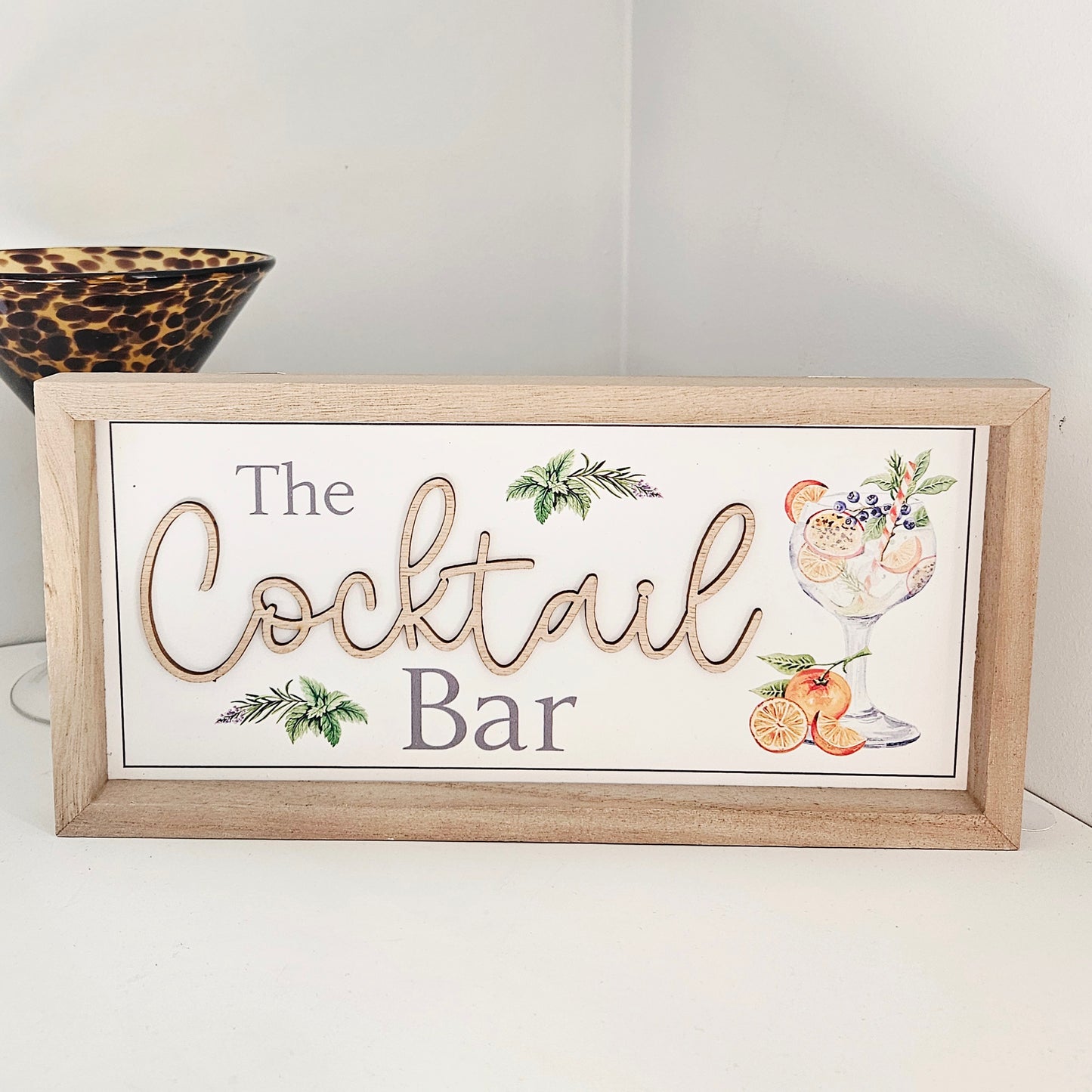 Decorative sign with 'The Cocktail Bar' text and cocktail illustrations on a white background.