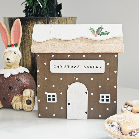 A decorative wooden house sign with 'CHRISTMAS BAKERY' on the front