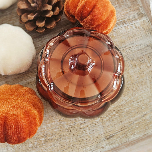 A small amber-brown glass pumpkin shaped candle with a scalloped rim and lid, for autumn scent 