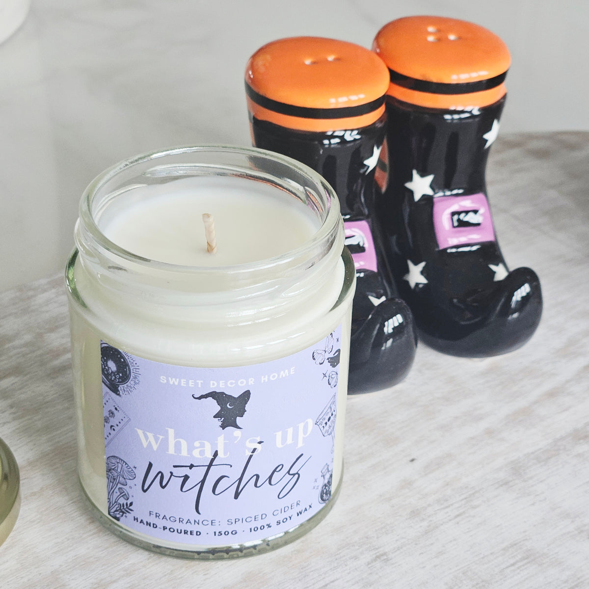 A glass jar candle labeled 'what's up witches' by Sweet Decor Home, spiced cider