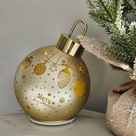 A decorative Christmas bauble ornament-shaped light in a frosted champagne-gold color with gold foil patterns and the words 'Merry Christmas' on the front. It has a metallic gold cap with a hanging loop 