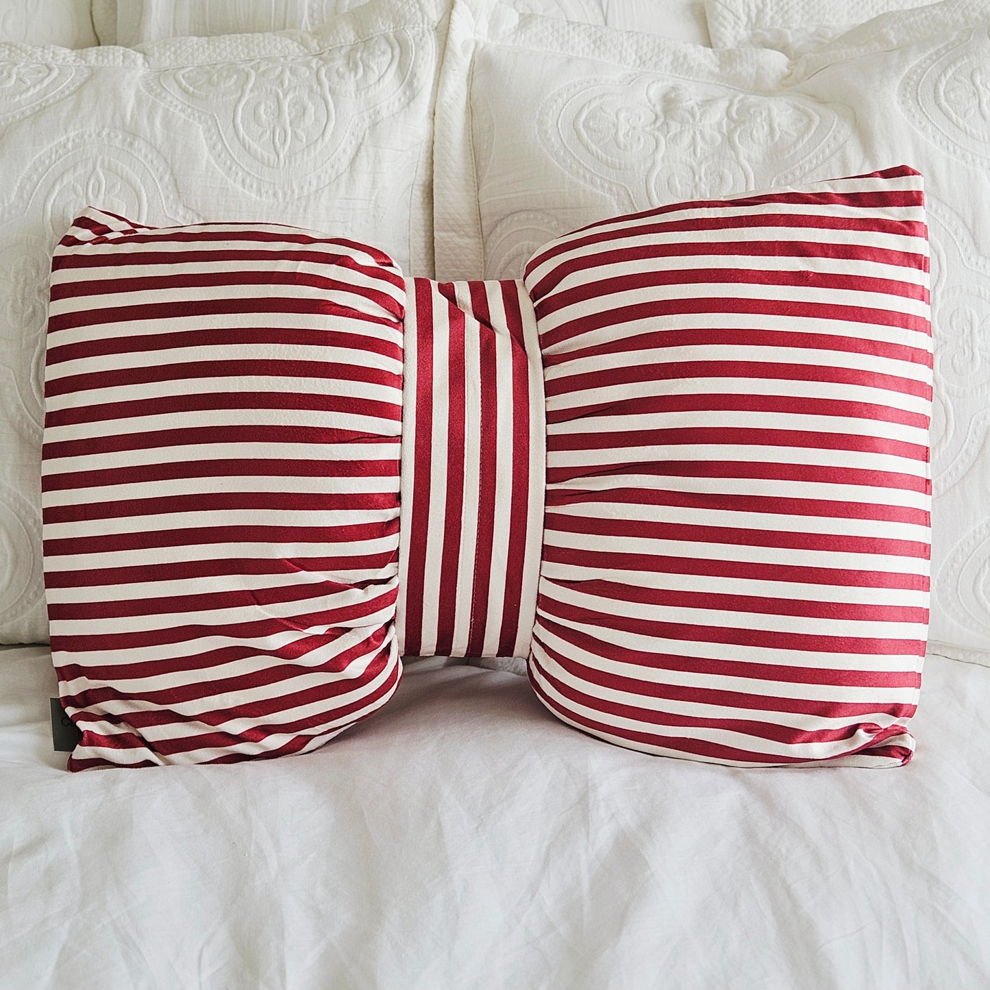 A decorative throw pillow shaped like a bow, featuring red and white horizontal stripes, in candle cane colours