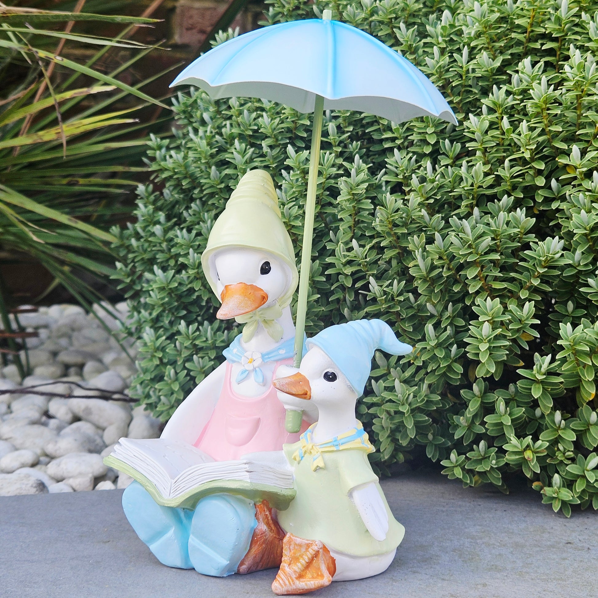 Decorative figurines of ducks in pastel colours under a blue umbrella reading a book