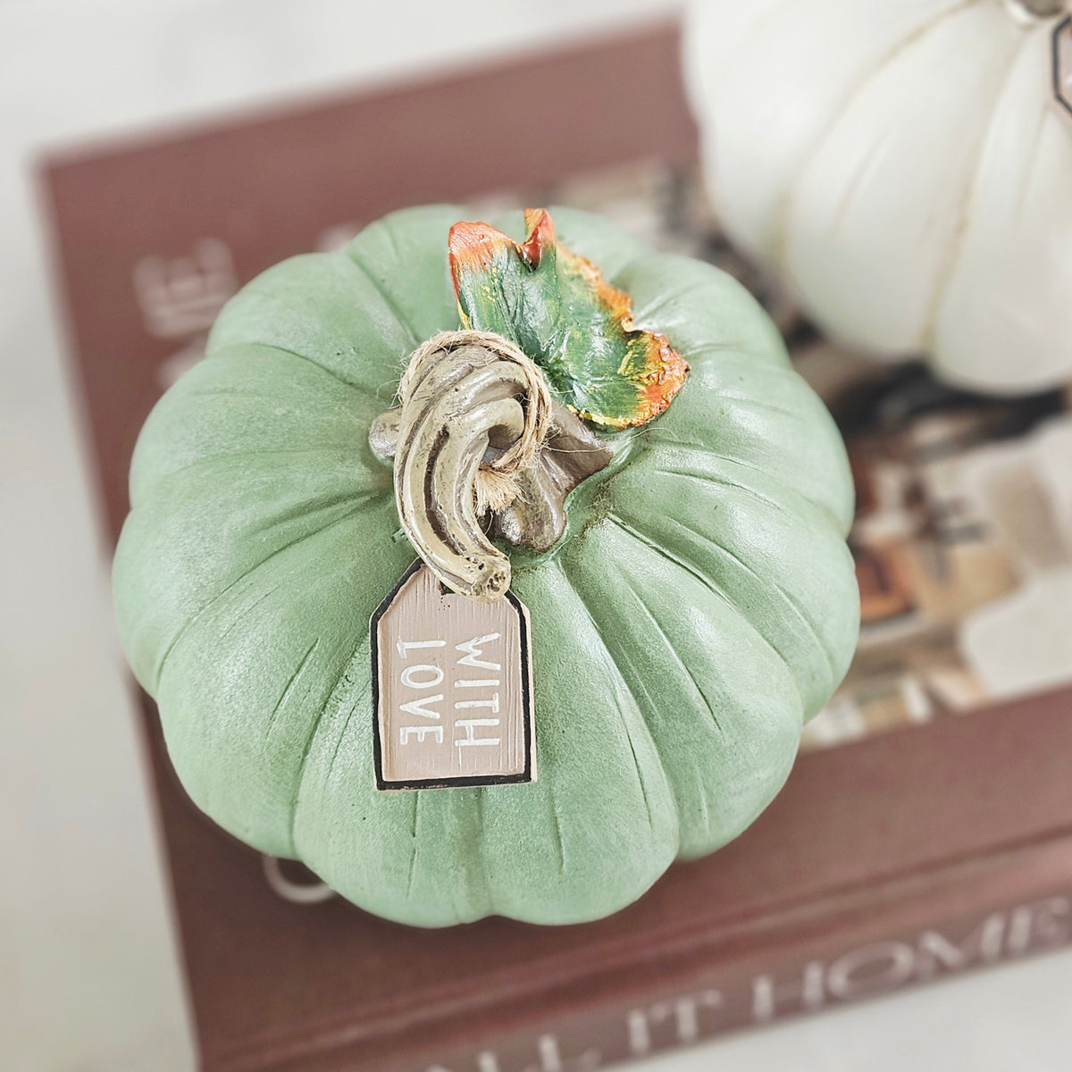 A mint green decorative faux pumpkin ornament with a textured stem and a hanging tag that reads 'WITH LOVE', styled on top 