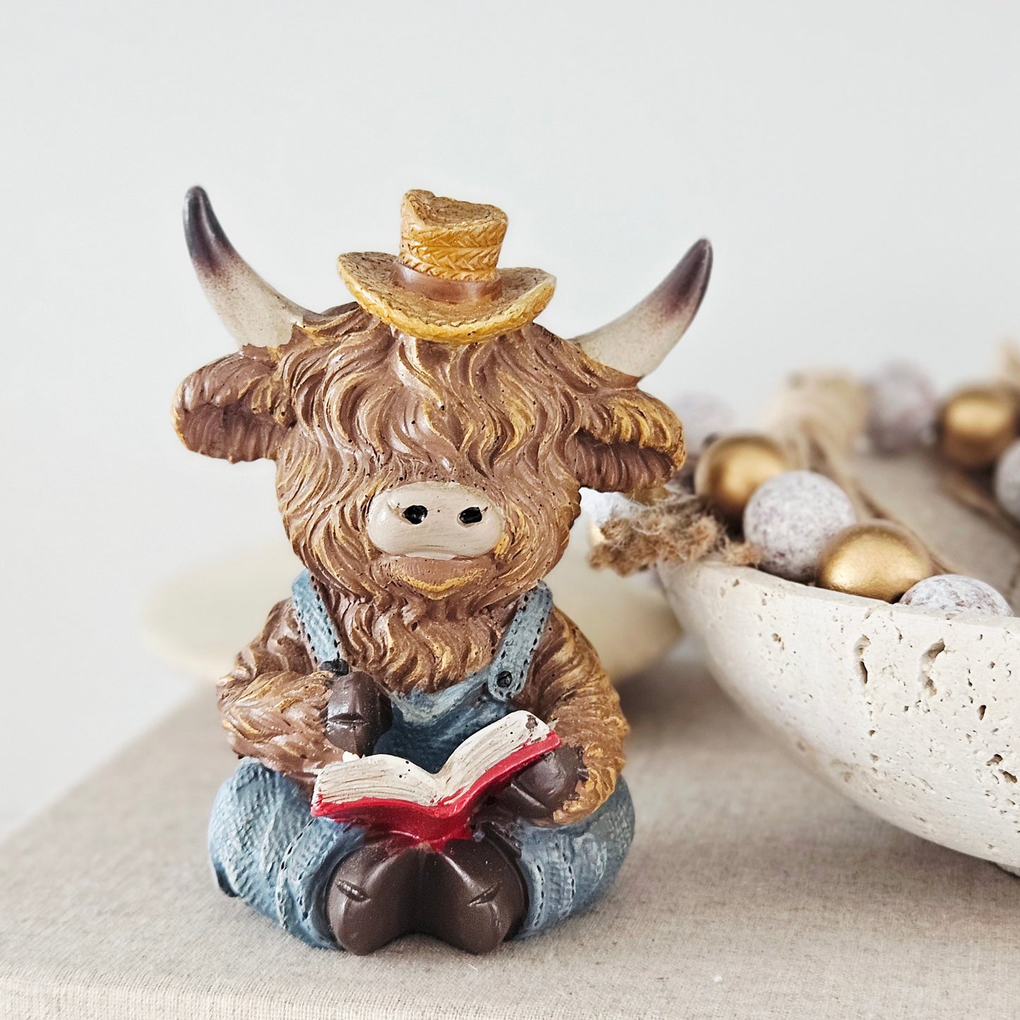 Figurine of a Highland cow reading a book with a top hat